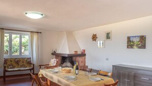 Un coin repas avec une table dressée pour quatre personnes, une cheminée et un banc agrémenté d’un coussin à motifs floraux.