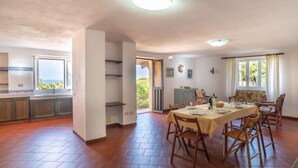 Une cuisine spacieuse avec un grand îlot central, un coin repas avec une table et des chaises, et une vue sur l’extérieur, accessible par un passage.