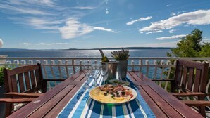 A table with a plate of food, a bottle, and glasses, set against a scenic view of the sea and sky.