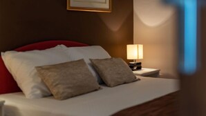A hotel room with a bed, pillows, a nightstand with a lamp, and a framed picture on the wall.