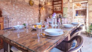 Un'accogliente sala da pranzo in stile rustico, con una parete in pietra, travi in legno e un lungo tavolo apparecchiato per un pasto.