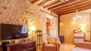 Una stanza accogliente con parete in pietra, travi in legno, televisore, divano, tavolo con candela e un piccolo mobiletto.