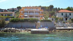 Un bâtiment situé sur la côte, doté de nombreux balcons, d’un mur en pierre et d’une jetée qui s’avance dans l’eau.