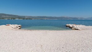 Une plage de galets avec une eau cristalline et des montagnes qui se dessinent à l’horizon.