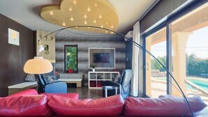 Un salon moderne avec un canapé en cuir rouge, un téléviseur et une vue sur la piscine.
