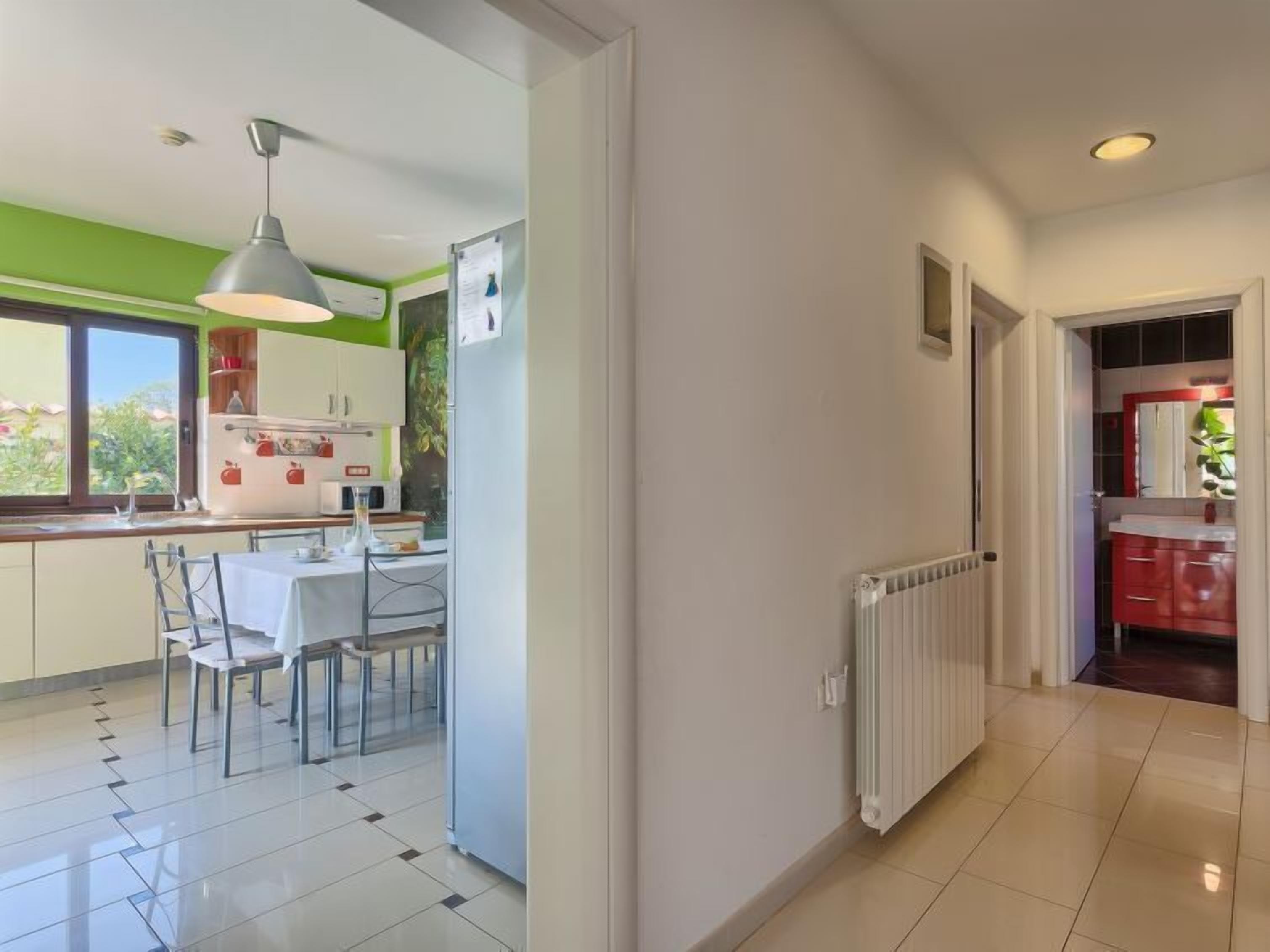 A modern kitchen with white cabinets, a dining table with chairs, and a hanging light fixture.
