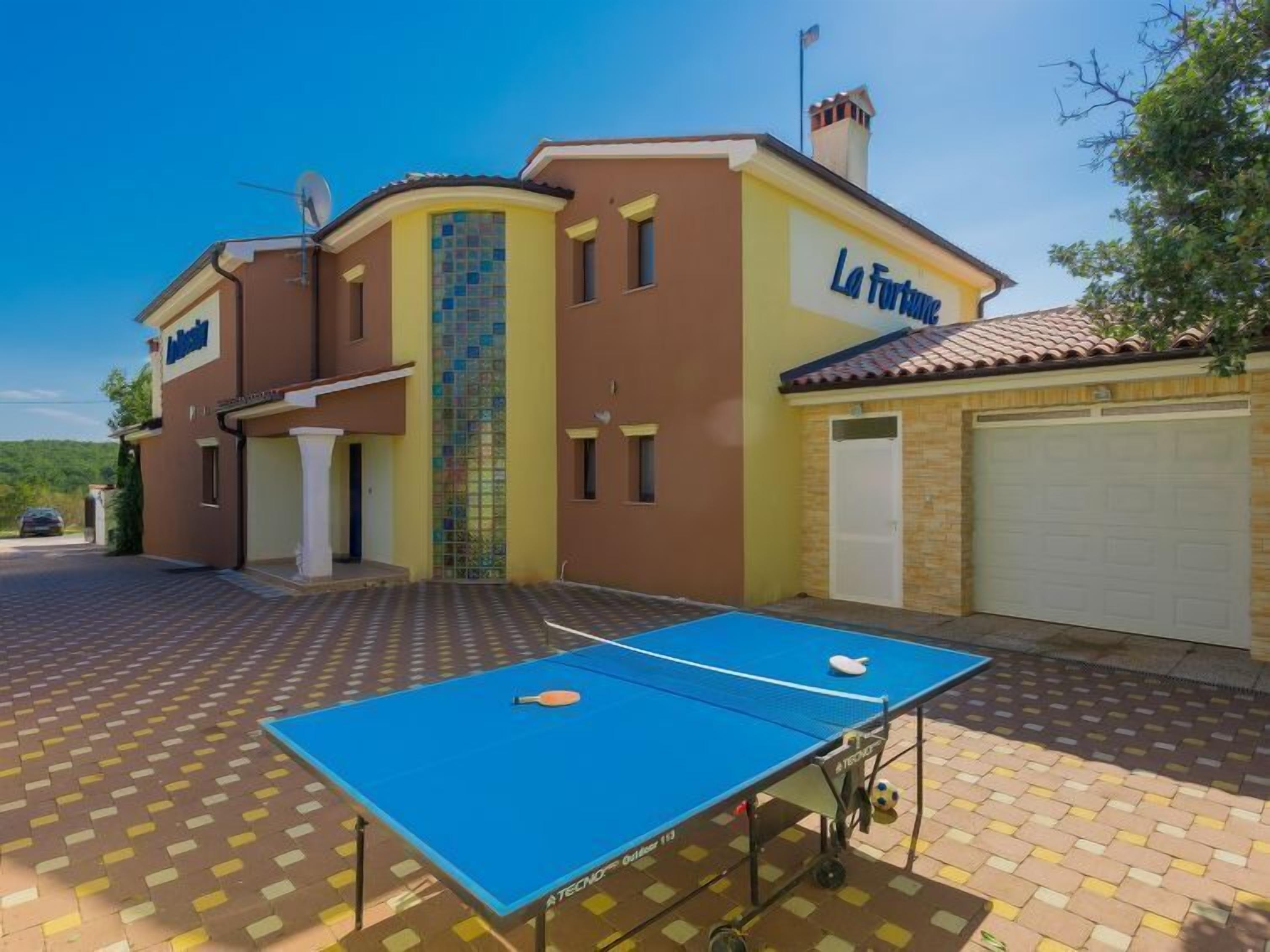 Un edificio con una mesa de ping pong azul en primer plano, un garaje y un letrero que dice "La Fortuna".