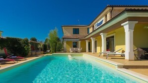 Une piscine à l’eau d’un bleu limpide, entourée d’un bâtiment à la façade jaune et sur lequel on peut lire l’inscription « L’Annucci ».