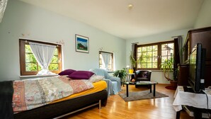 Ein gemütliches Zimmer mit einem Bett, einem Sessel, einem Fernseher und einem Fenster mit Vorhängen.