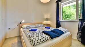 Ein Schlafzimmer mit einem Bett, Nachttischlampen, einem Fenster mit Vorhängen und einer Steckdose an der Wand.