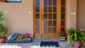Eine Holztür mit Fensterteil, darüber ein kleines Fenster und eine Topfpflanze links.