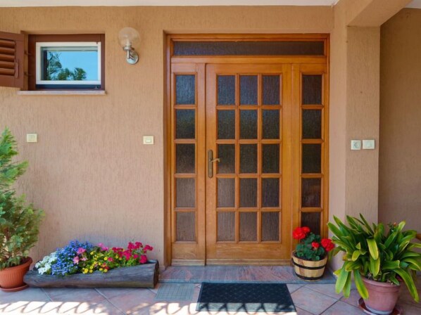 Una puerta de madera con un panel de vidrio, una pequeña ventana encima y una maceta a la izquierda.