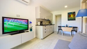 Ein modernes Wohnzimmer mit Flachbildfernseher, einer Couch, einem Esstisch mit Stühlen, einer Küchenzeile und einem Bild an der Wand.