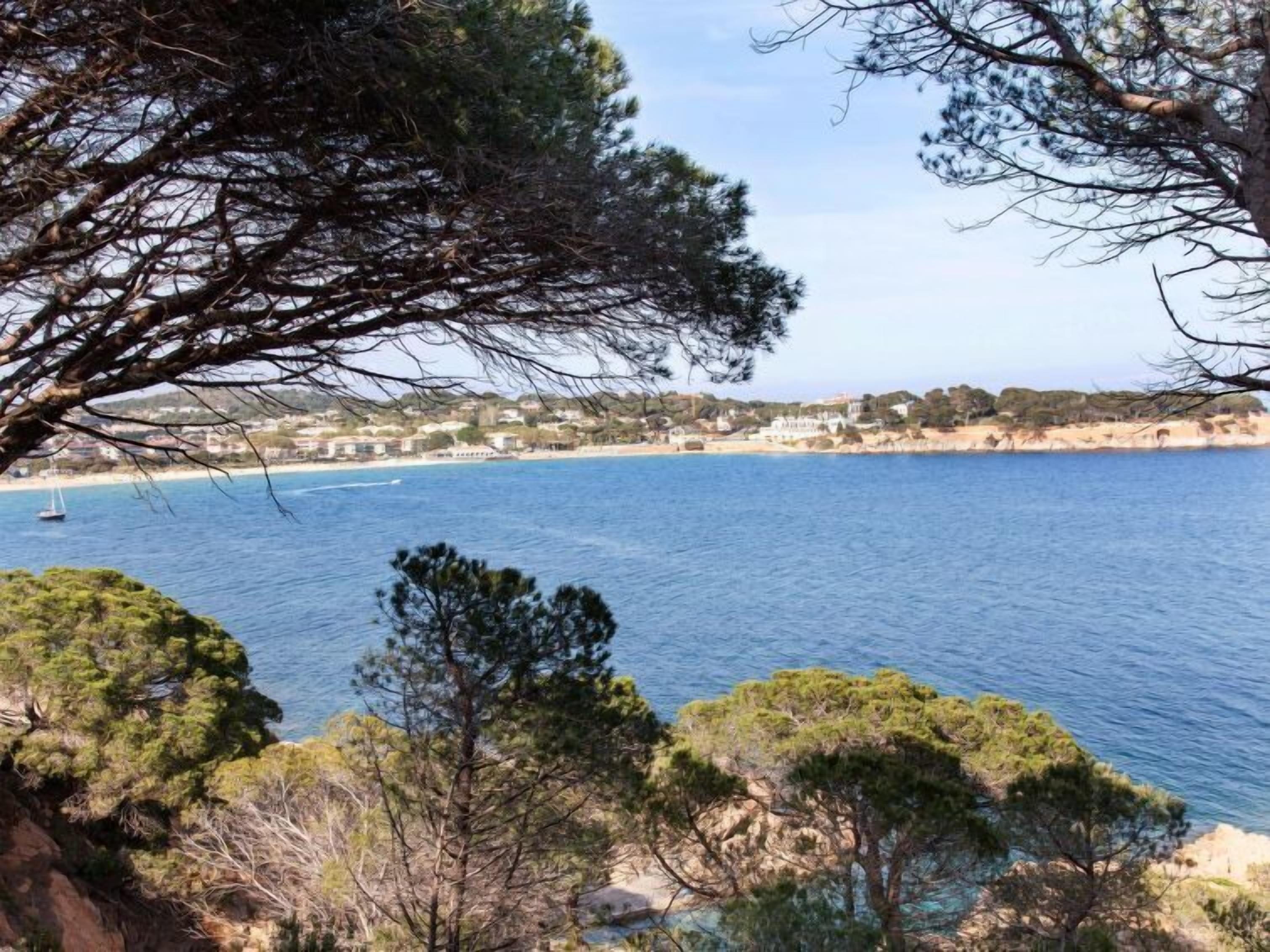 Une vue sur la côte, avec une mer bleue et limpide, un bateau au loin et une ville en arrière-plan.