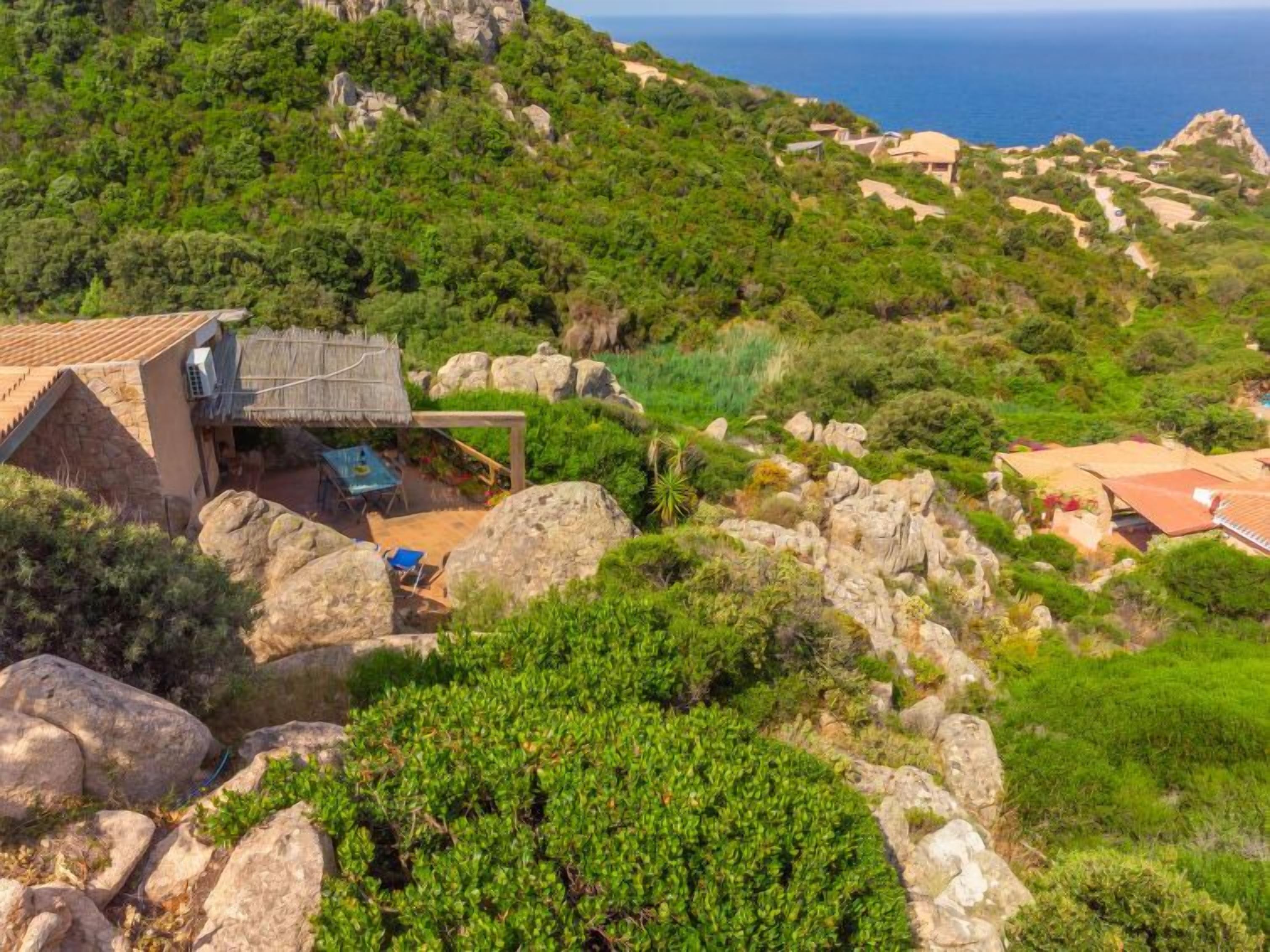A hillside property with a stone house, outdoor seating, and a view of the sea.