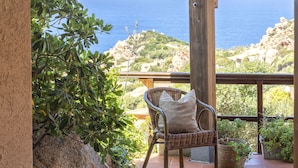 A wicker chair with a cushion on a balcony overlooking the sea.