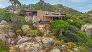 A modern house with a patio, surrounded by rocky terrain and greenery.
