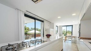 Une cuisine moderne dotée d’un grand îlot central, de grandes fenêtres et offrant une vue sur l’extérieur.