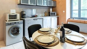 Une cuisine compacte équipée d’un lave-linge, d’un four à micro-ondes et de placards. On y trouve une table à manger, mise avec des assiettes, des verres et une bouteille.