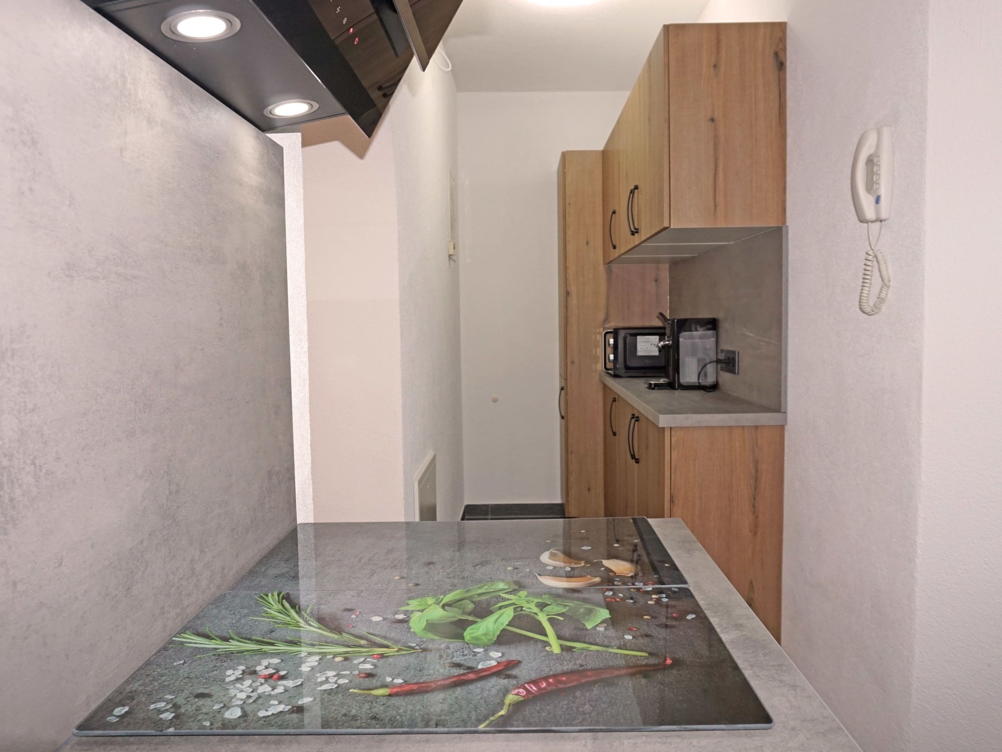 A kitchen with a countertop, wooden cabinets, a microwave, and a phone on the wall.