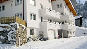 A multi-story building with a stone foundation, wooden balconies, and a snow-covered landscape. - Apartment Susi by Interhome (Flirsch)