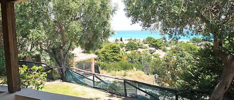 A covered outdoor seating area with a view of a coastal landscape, including trees and a distant beach.