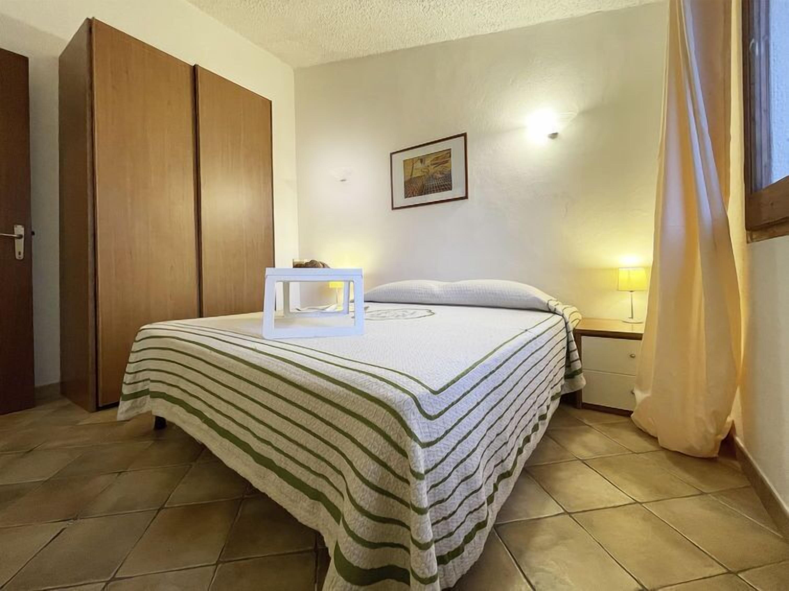 Ein ordentlich bezogenes Bett mit gestreifter Bettdecke, ein Nachttisch mit Lampe und ein Holzschrank.