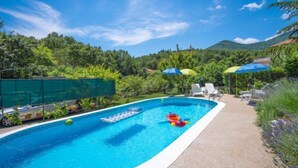 A swimming pool with a clear blue water, surrounded by greenery and a path leading to lounge chairs. - Vacation home Zorica by Interhome (Opatija/Mihelici)