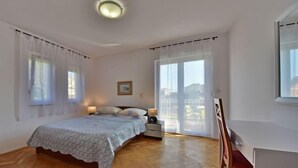 A bedroom with a bed, bedside tables, a chair, and a large window with curtains. - Vacation home Zorica by Interhome (Opatija/Mihelici)