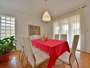 A dining area with a red tablecloth, white chairs, a potted plant, and a painting on the wall. - Vacation home Zorica by Interhome (Opatija/Mihelici)