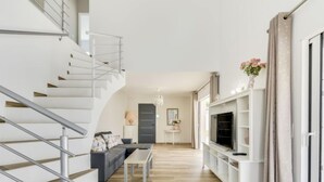 En moderne stue med trappe, sofa, sofabord og fjernsyn.