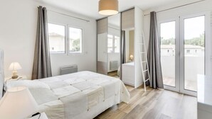 Et moderne soveværelse med en stor seng, et skrivebord og udsigt over byen gennem store vinduer.