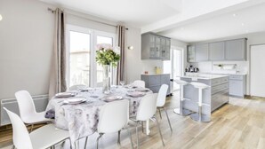 Et moderne køkken med lysegrå skabe, en central ø og et spiseområde med et marmorbord og hvide stole.