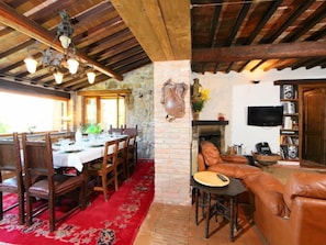 Zona pranzo con tavolo e sedie in legno, tappeto rosso e parete in pietra.