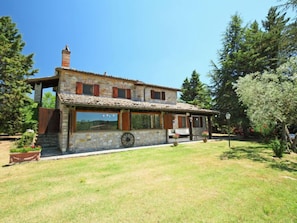 Una casa di pietra con tetto in tegole, persiane di legno e una carriola nel cortile.