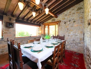 Zona pranzo con parete in pietra, travi in legno al soffitto e tappeto rosso.