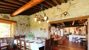 Un comedor rústico con pared de piedra, vigas de madera en el techo y una araña.