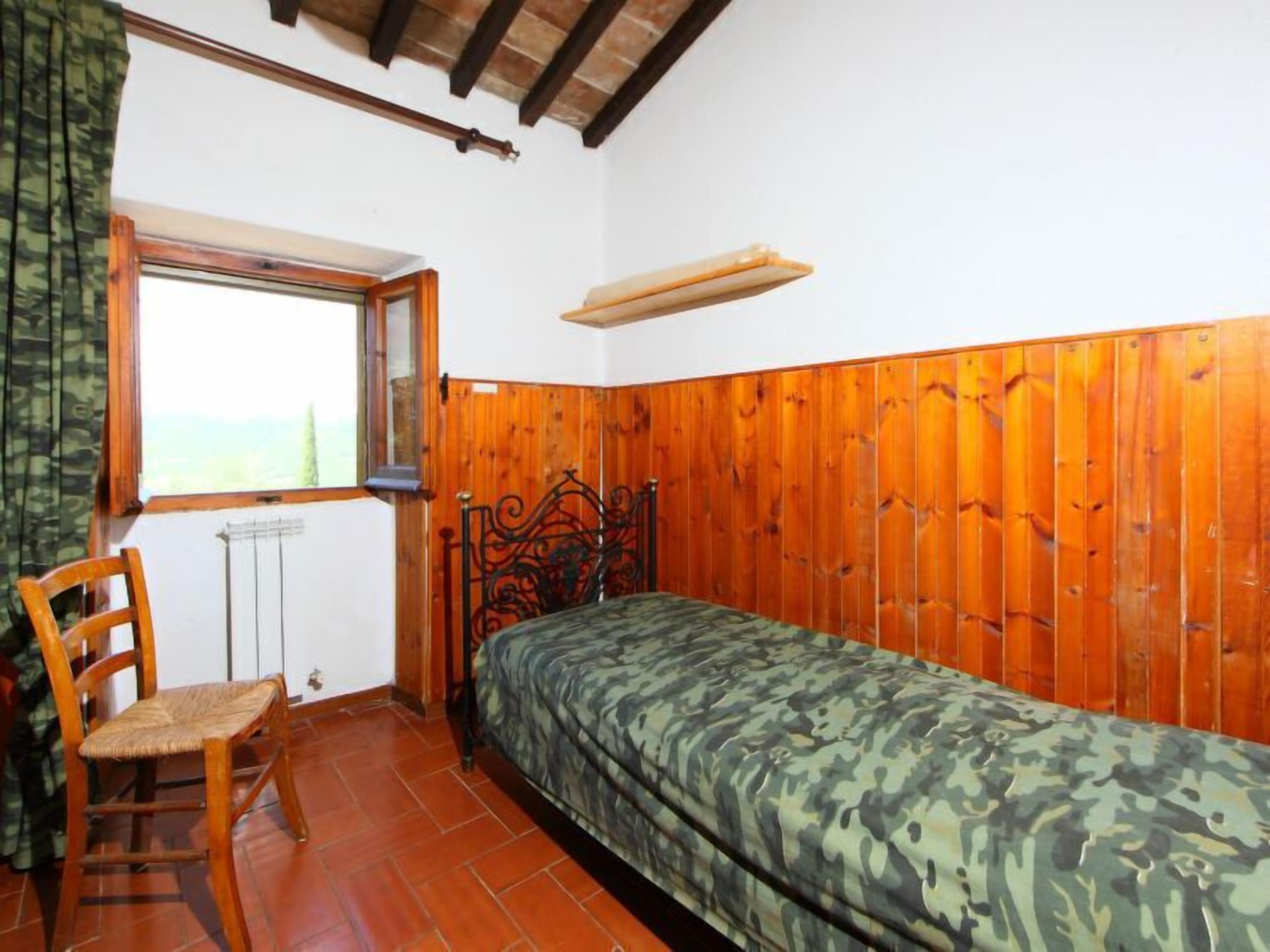 A bedroom with a wooden bed, a chair, a window, and a radiator.
