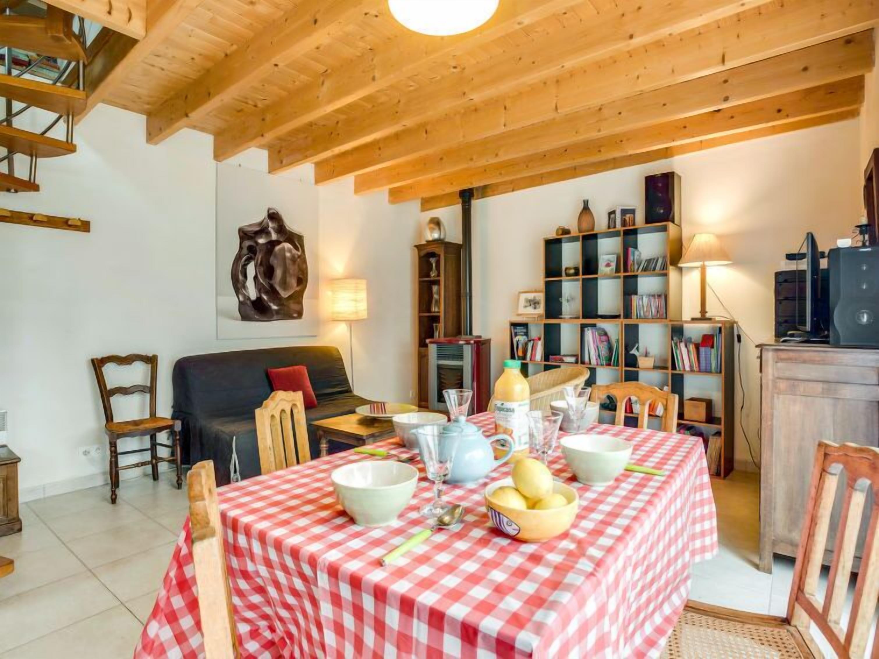 A cozy dining area with a checkered tablecloth, wooden chairs, and a bookshelf filled with books.