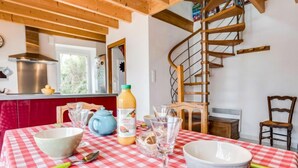 Eine Küche mit kariertem, rot-weißem Tischläufer, einer Wendeltreppe aus Holz und einem Fenster mit Blick auf Grünflächen.