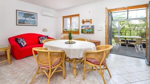 Un coin repas avec une table ronde, des chaises en osier et un canapé rouge.