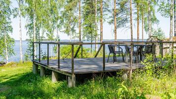 A wooden deck with chairs overlooking a lake, surrounded by trees.