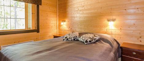 Una camera in legno con un letto, due lampade ai comodini e una finestra con persiane.