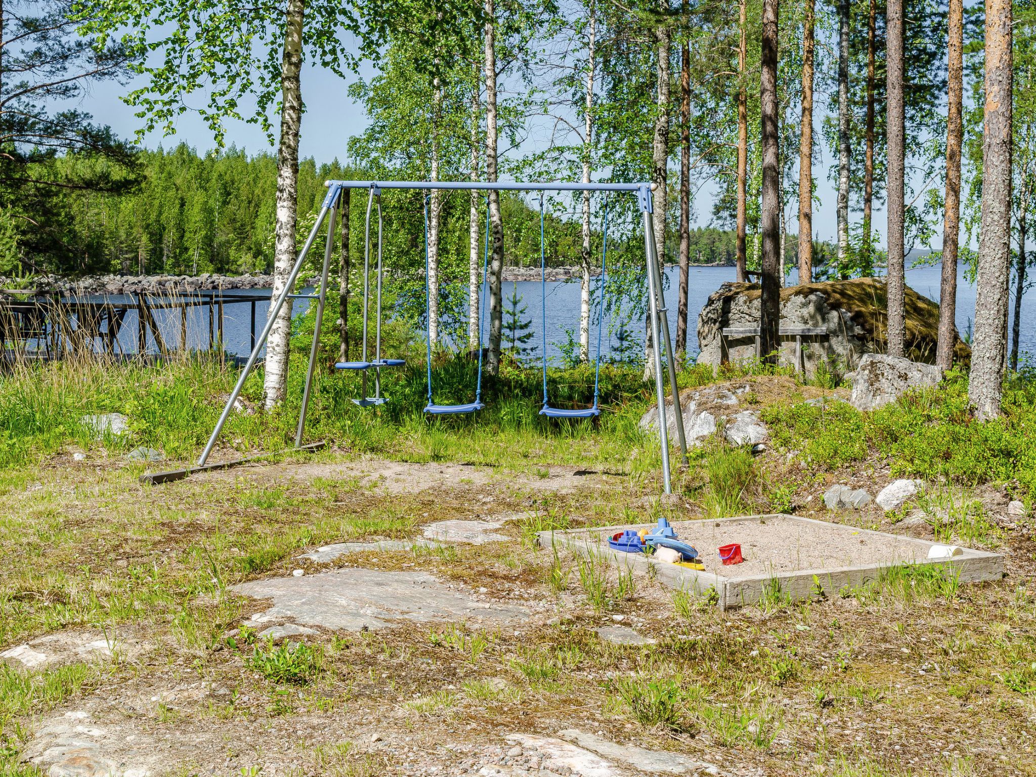 A swing set in a natural setting with a lake and trees in the background.
