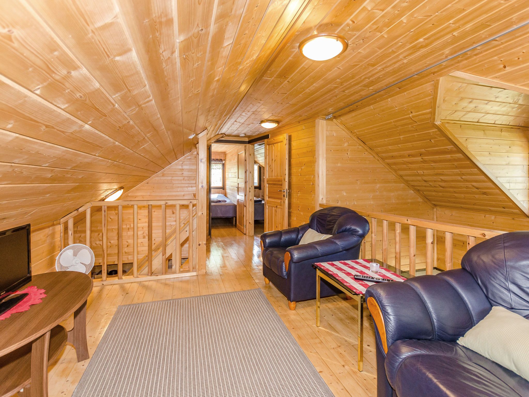A wooden interior with a loft bedroom, a sofa, a table, and a fan.