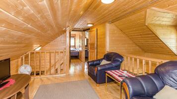 A wooden interior with a loft bedroom, a sofa, a table, and a fan.