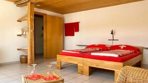A wooden bed with red bedding, a wicker chair, a small table with glasses, and a red towel on the wall.