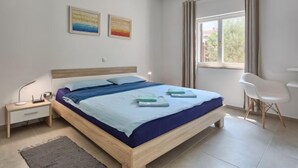Een moderne slaapkamer met een houten bed, een bureau en een stoel. Twee schilderijen hangen aan de muur en er is een raam met gordijnen.