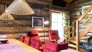 A log cabin interior with a dining area, red upholstered chairs, a wooden table, and a staircase.