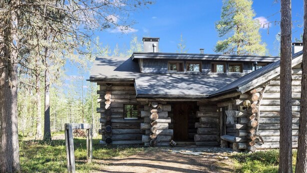A log cabin with a stone foundation, a chimney, and a porch with a bench.